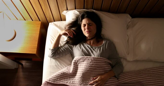 Worried woman unable to sleep suffering from insomnia. Person tossing and turning turning nightstand light ON