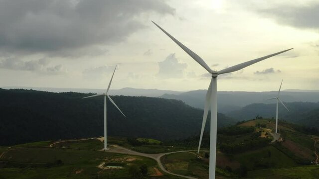 Aerial view, windmills rotating by the force of the wind and generating clean renewable energy for sustainable development in a green ecologic way on cloudy sky at dusk. The look up shot by drone