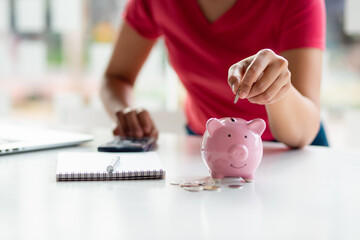 Closeup of female hand putting money coin into piggy bank for saving money. saving money and...