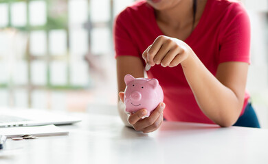 Obraz na płótnie Canvas Closeup of female hand putting money coin into piggy bank for saving money. saving money and financial concept