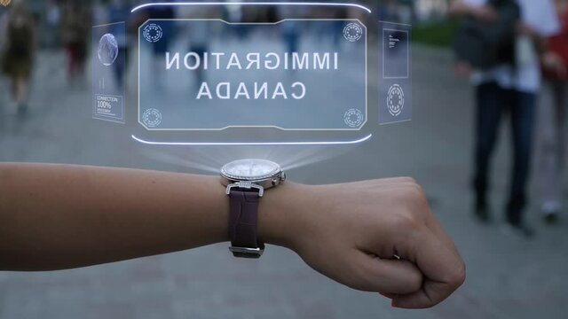 Female hand with futuristic smartwatch interacts HUD hologram with text Immigration Canada. Woman uses holographic technology on wristwatch against the background of evening city with people