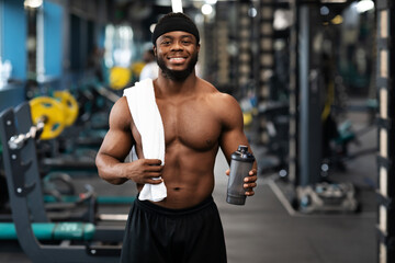 Fototapeta na wymiar Happy black bodybuilder with water and towel at gym