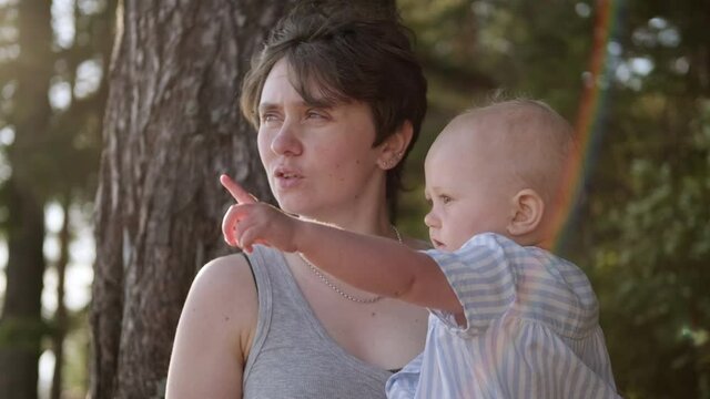 A young mother plays and hugs with her baby daughter outdoors. Summer and sunset at the bay. A natural park.