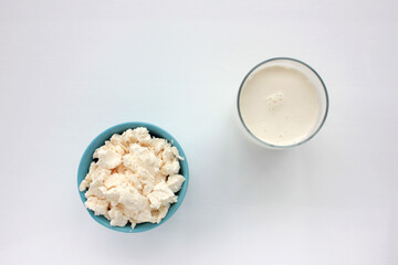 Cottage cheese in blue bowl glass of milk on white table. Homemade ricotta. Top view. Copy space.