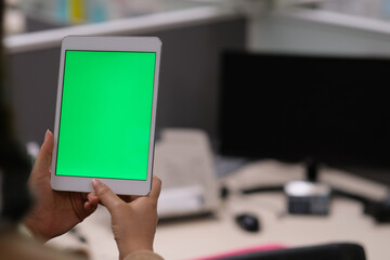 over the shoulder view of woman using green screen tablet in office