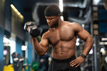 Fototapeta na wymiar Handsome black athlete training arms with dumbbells at gym