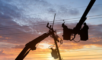 Silhouette electrician works on bucket car to maintenance high voltage transmission lines.