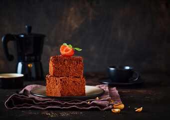 Stack of pieces or bar of chocolate cake brownie with strawberries and pistachio nuts on the black background, selective focus image.