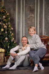 adult beautiful woman and man are sitting on the sofa near the christmas tree