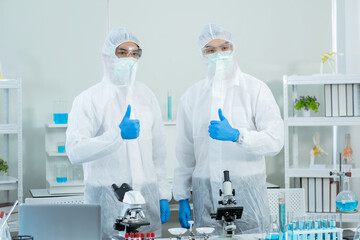 Two scientists wearing personal protective and safety glass standing and thumb up in the laboratory. Research on the coronavirus vaccine to prevent COVID-19. Medical and health concept.
