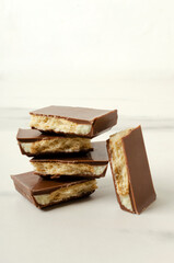 Stack of milky chocolate with crunchy cookies on the white marble table.Vertical image