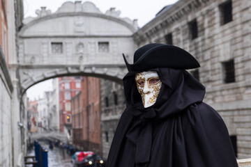 Fototapeta na wymiar Venice, Italy - February 17, 2020: An unidentified person in a carnival costume in front of Ponte dei Sospiri, attends at the Carnival of Venice.