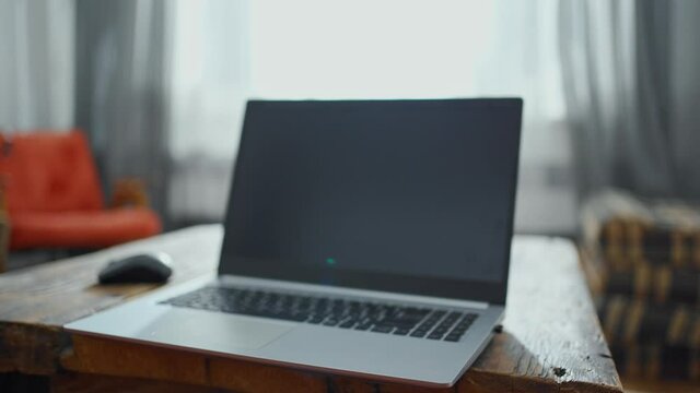 blurred image of home workspace in living room with laptop and old vintage handmade wooden table. Minimalistic Interior with natural wooden materials. laptop with blank screen and mouse on table