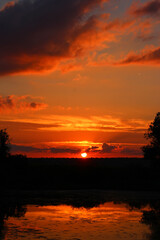 Saturated red sky at sunset sun, scenic panorama with river and clouds
