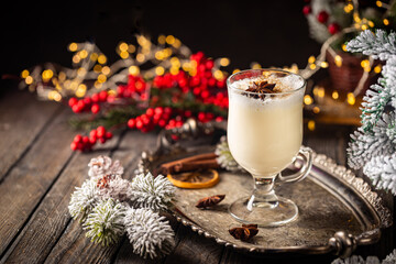 Traditional winter eggnog in a glass mug with milk, rum and cinnamon, christmas decorations