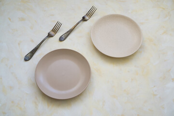 Plates and cutlery on a light surface. Table setting for two people with forks.