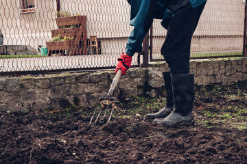 Villager in a blue black jacket and black rubber boots puts manure in the dirt for a better...
