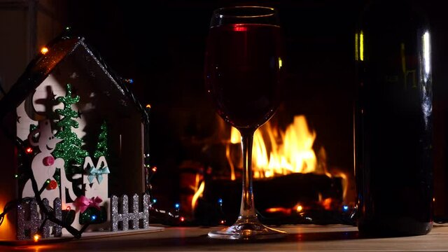 Holiday season. Christmas decorations, a glass with a drink and a bottle on the background of the fireplace flame. Panning. Close-up shooting.