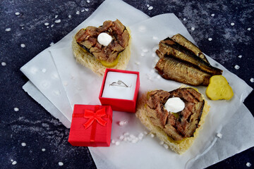 Gift box with red ribbon and heart on medical mask with sprat sandwiches on concrete black...