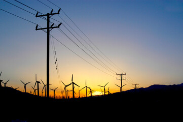 Windmill farm in the desert at sunset in Palm Springs, California with power lines going to the...