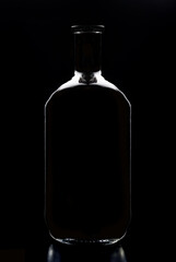 An empty liquor bottle in silhouette with reflection, isolated on black.