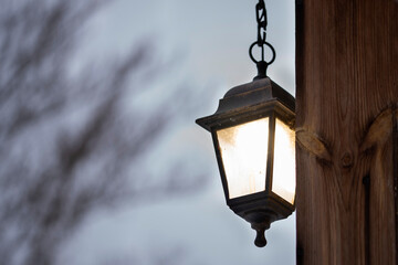 Fototapeta na wymiar An old lantern shines on the wall against the overcast evening sky