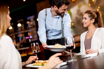 Young waiter serving food to female customers in the restaurant