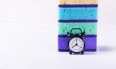 Small alarm clock and the stack of multicolored sponges. Time for general cleaning up. Copy space