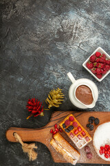 top view different berry cakes on chopping board xmas toys bowls of raspberries liquid chocolate on grey-white background with copy space