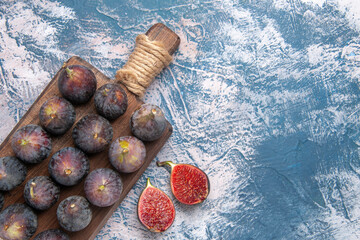 Above view of full fresh black mission figs split ones on wooden cutting board on gray background
