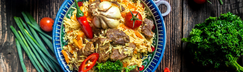 Traditional uzbek meal called pilaf. Rice with meat, carrot and onion in plate with oriental ornament, Uzbek oriental cuisine. Long banner format. space for text