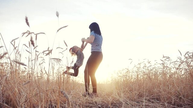 mom play with her daughter the park in wheat field. happy family people in the park concept. mom play is spinning daughter holding hands in wheat field. childhood dream happy family fun