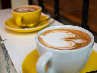 APPETIZING COFFEE DECORATED WITH MILK, IN A YELLOW AND WHITE CUP
