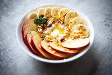 Oatmeal with banana, nuts, apple and honey in white bowl closep. Natural health dieting food