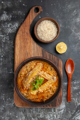 top view a bowl of chicken soup on chopping board wooden spoon a bowl of rice lemon slice on dark background