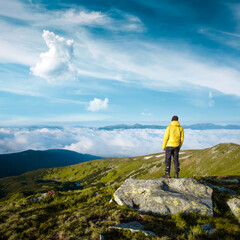 Alone tourist in yellow jacket stay on rock on high mountains. Landscape photography