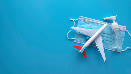 Travel and healthcare concept. Top view of face mask, hand sanitizer, and toy plane isolated on blue background with copy space.
