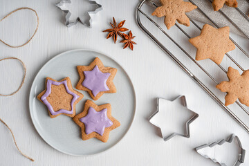 Decorating of sweet savory ginger cookies or gingerbread with violet icing on gray plate cooked for christmas winter holidays on white wooden table with cutters, anise and grate. Horizontal, flat lay