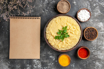 top view mashed potatoes in wooden bowl sea salt black pepper red pepper turmeric in small bowls a notebook on dark background