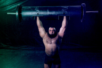 a bearded strongman raised a large metal log above him
