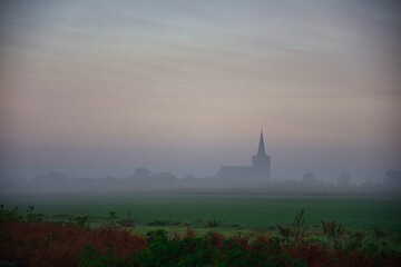 foggy morning with a view of wet fields and in front of the small Dutch village. Morning dew in the...