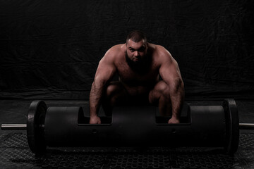 the bearded strongman crouched down and prepares to lift a large metal log