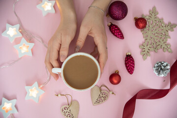Composition of Christmas toys, balloons, garlands. Female hands holding a Cup of coffee on a dark background, top view.