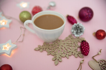 Obraz na płótnie Canvas A composition of Christmas decorations, Christmas balls, toys, garlands and a Cup of coffee for a pleasant pastime on a pink background.