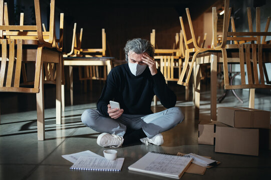 Frustrated Owner Sitting On Floor In Closed Cafe, Small Business Lockdown Due To Coronavirus.