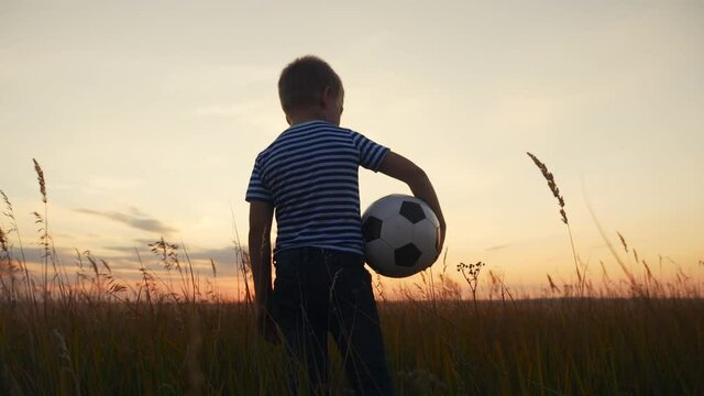 Childhood dream. boy holding soccer ball walking in the park silhouette. happy family kid dream concept. kid boy walking on the field silhouette at sunset carries a soccer ball fun. baby winner
