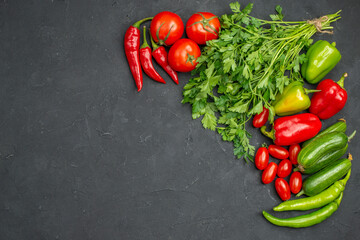 Top view of fresh vegetables and a bunch of green on the left side on dark table