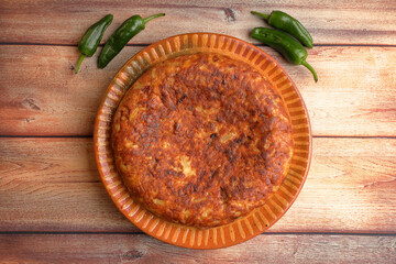 Tortilla de patatas (Spanish omelette) garnished with grilled green peppers, on wooden table
