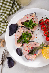 Fresh organic seafood. Raw sturgeon steaks on a white plate with spices and vegetables. On a gray...
