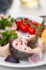 Fresh organic seafood. Raw sturgeon steaks on a white plate with spices and vegetables. On a gray background. Side view